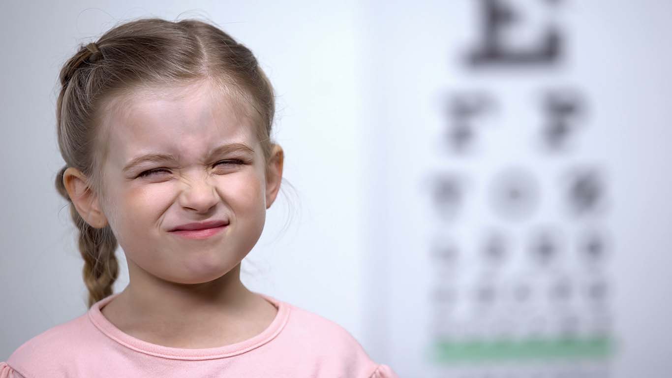 En pige, der kniber øjnene sammen pga. sløret syn. Synsudvikling hos børn.