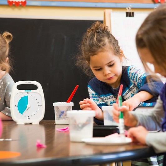 Time Timer Plus 20 minutter. Barn sidder ved et bord.